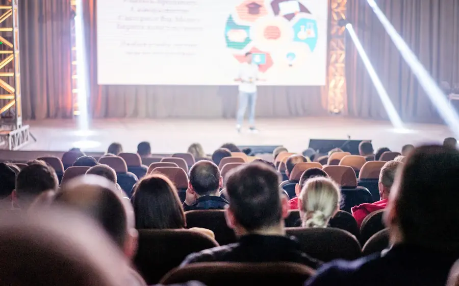 Audience in a dark auditorium watching a presentation on stage