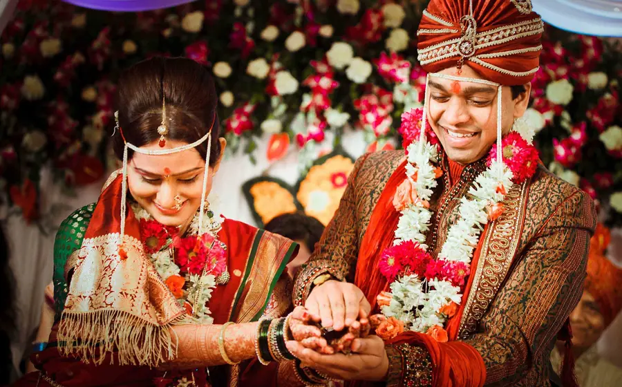 Bride and groom in red and gold with flower garlands during the wedding ceremony