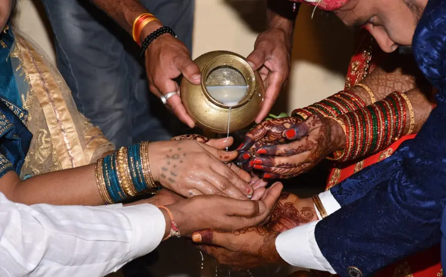 Family hands pouring water from a brass kalash during a wedding ritual