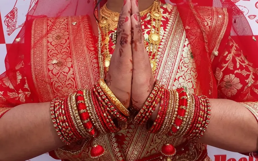 Bride in red with wedding bangles and henna, hands joined in namaste