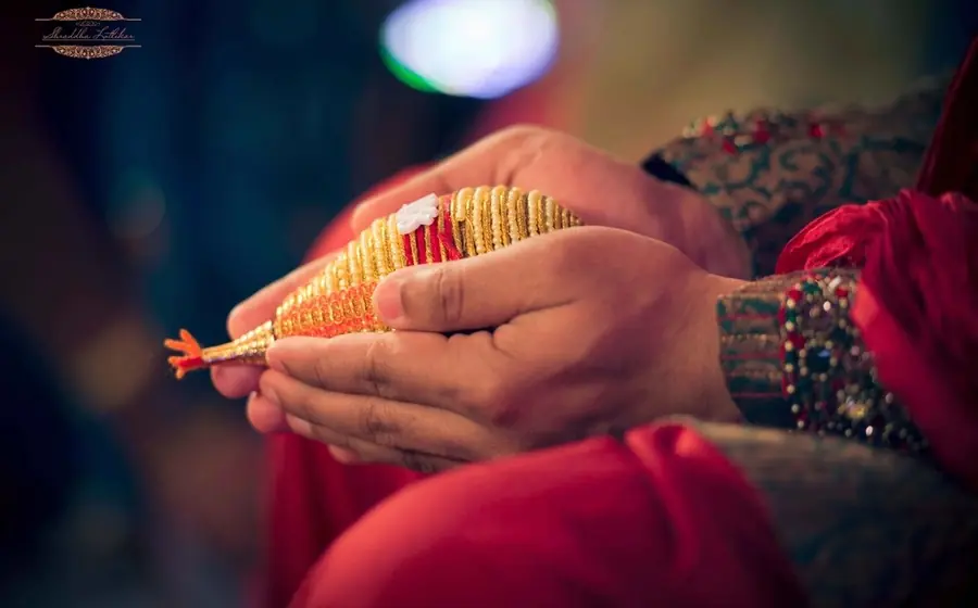 Hands holding a decorated red and gold wedding item during a ritual